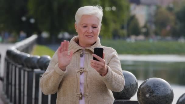 Overblij senior Kaukasische vrouw oma zwaaiende hand het maken van videogesprek kijken naar smartphone camera praten op moderne mobiele telefoon, gelukkig volwassen dame van middelbare leeftijd spreken hebben aangename communicatie - Video