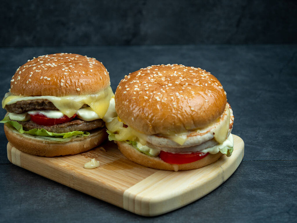 Hovězí burger se salátem, sýr na řezací desce na černém dřevěném stole. - Fotografie, Obrázek