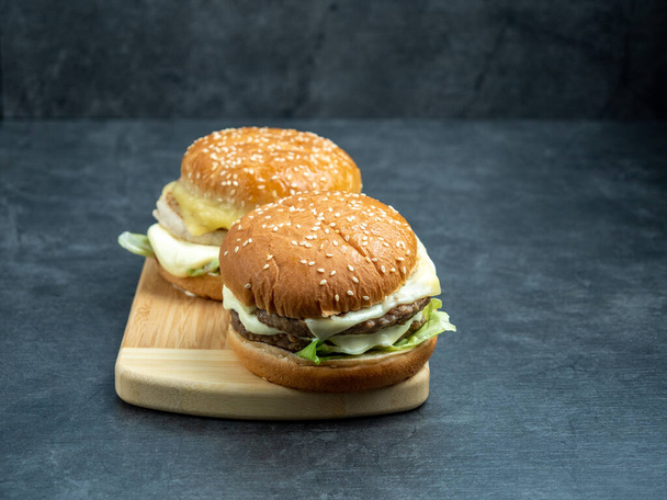 Beef burger with salad, cheese on a cutting board on a black wooden table. - Foto, afbeelding