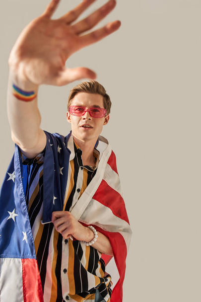 Muž natahuje ruku k fotoaparátu a hrdě drží americkou vlajku při pózování - Fotografie, Obrázek