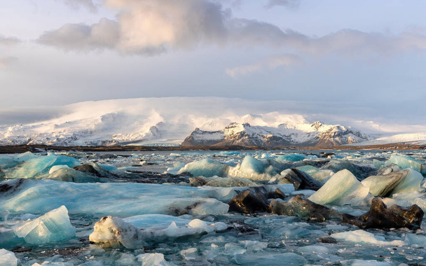 Jéghegyek a Jokulsarlon gleccserlagúnában, a Vatnajkull Nemzeti Parkkal határos Délkelet-Izlandon, részben Vatnajkull gleccser a környező hóval borított hegyekkel.  - Fotó, kép