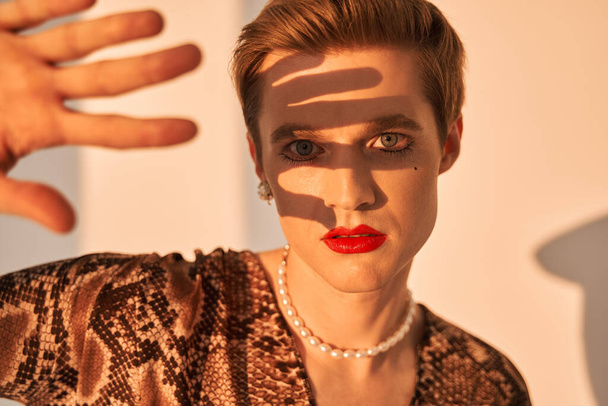 Gender fluid male with makeup and earrings covered from the sun with his hand - Zdjęcie, obraz