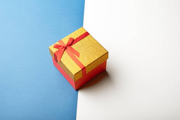Red and gold gift box with a ribbon on a bright two-colored background. Top view.  - Fotografie, Obrázek