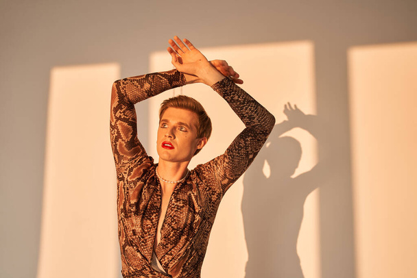 Man with drag queen makeup holding his hands up and looking away while posing - Zdjęcie, obraz