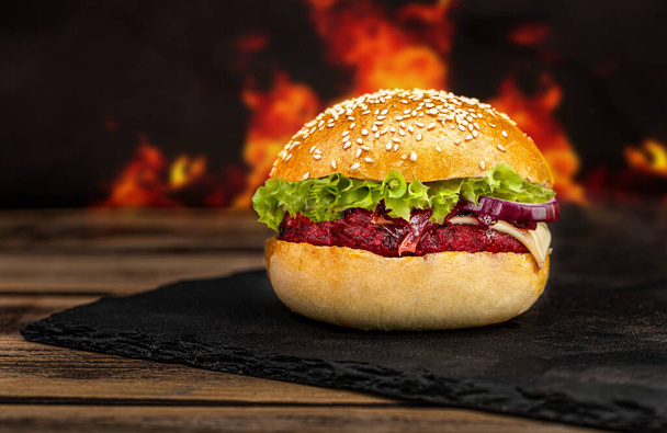Sabrosa comida callejera a la parrilla hamburguesa vegetariana de remolacha en pan crujiente con lechuga y aguacate en tablero de piedra negro - Foto, Imagen