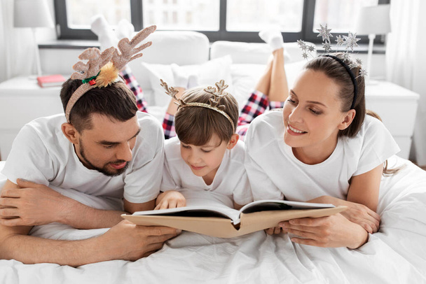 family with book in pajamas in bed on christmas - 写真・画像