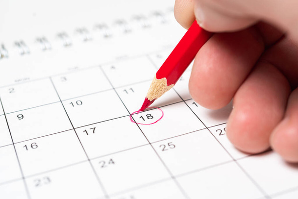 Person markiert das Datum mit rotem Bleistift als Erinnerung auf dem Kalender. - Foto, Bild