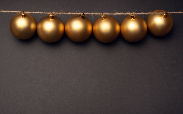 A row of gold Christmas balls hanging on a dark background - Foto, Imagem