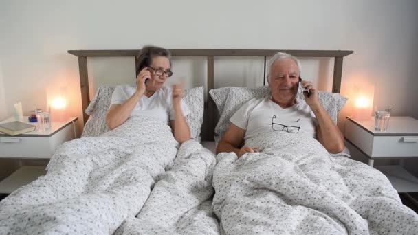 vanhempi ikääntyminen aviopari mies mies ja nainen lepää yhdessä sängyssä kotona asunnossa älypuhelimella kutsuva hymy - Materiaali, video