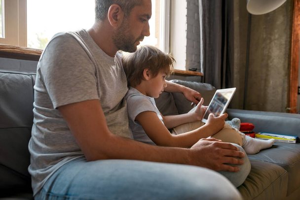 Caucasian father relax at home with son using tablet - Foto, imagen