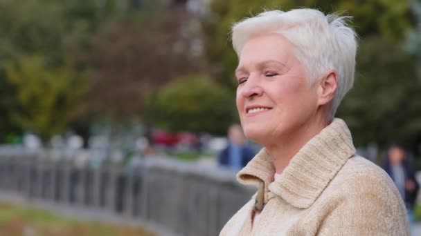 Happy mature middle aged single woman turns his head slowly looking at camera posing for video portrait, smiling older gray-haired female, healthy cheerful senior retired lady with beautiful face - Footage, Video