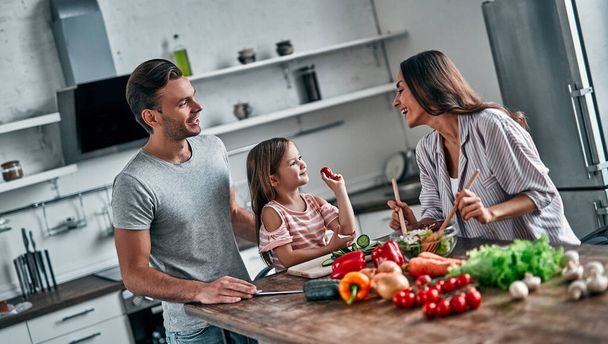 Mom, dad and daughter are cooking on kitchen. Happy family concept. Handsome man, attractive young woman and their cute little daughter are making salad together. Healthy lifestyle. - Foto, immagini