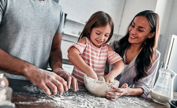 Cute little girl i jej pięknych rodziców są ugniatać zabawy mąki do pieczenia i uśmiech podczas gotowania w kuchni. - Zdjęcie, obraz