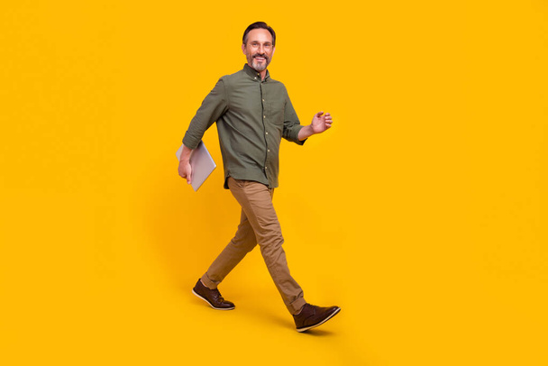Full length body size view of attractive cheerful man employer going carrying laptop isolated over vivid yellow color background - Fotoğraf, Görsel