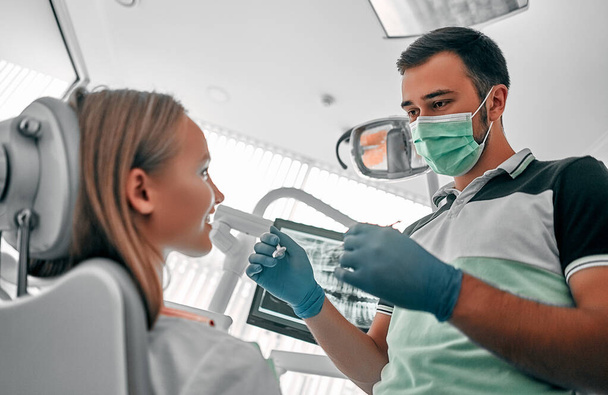 Mladý zubař pracuje, vyšetřuje a opravuje zuby na zubní klinice u pacientky s otevřenou pusou. Zdravé zuby koncept. - Fotografie, Obrázek