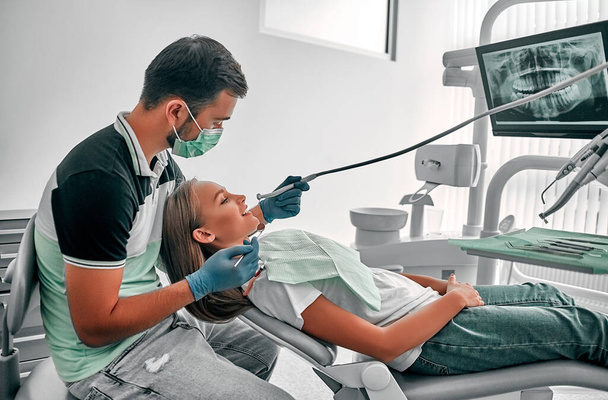 Dentysta bardzo dokładnie sprawdza i naprawia ząb swojej młodej pacjentki. Szczęśliwa młoda kobieta siedzi na krześle dentystycznym w gabinecie dentystycznym. - Zdjęcie, obraz