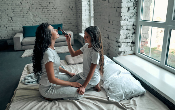 Happy loving family.  Mother and daughter doing your makeup sitting on the bed in the bedroom. - Fotografie, Obrázek