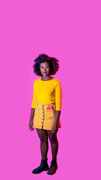 jovem preto mulher posando isolado olhando amigável e relaxado sorrindo positivo no rosa publicidade copyspace fundo - Foto, Imagem