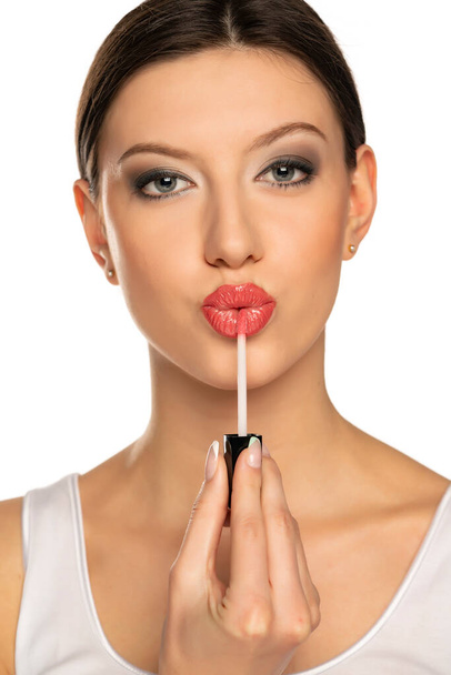Plan de la tête d'une femme appliquant un brillant à lèvres sur ses lèvres avec un geste de baiser sur un fond blanc - Photo, image