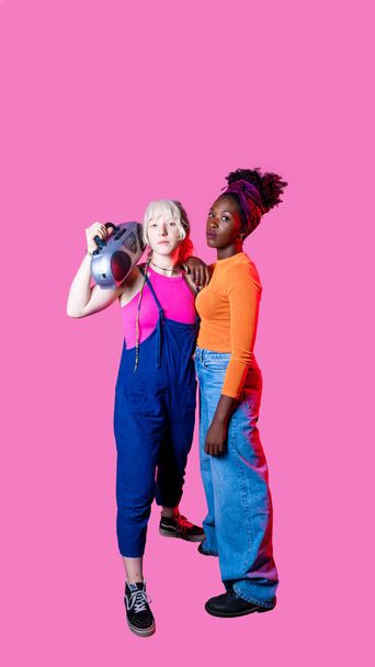 Twee jonge diverse vrouwen houden boombox poseren zelfverzekerde geïsoleerde copyspace reclame achtergrond - Foto, afbeelding