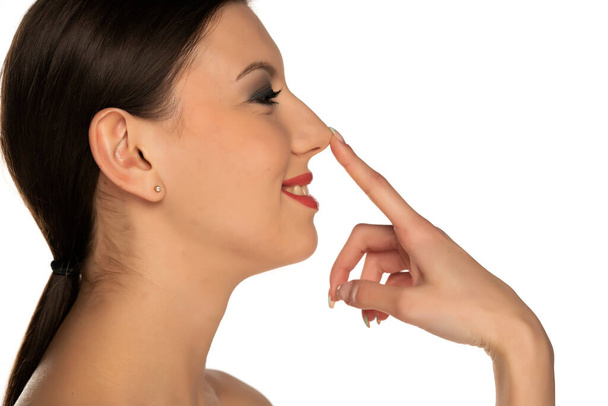 profil mladé usměvavé ženy dotýkající se jejího nosu na bílém pozadí - Fotografie, Obrázek