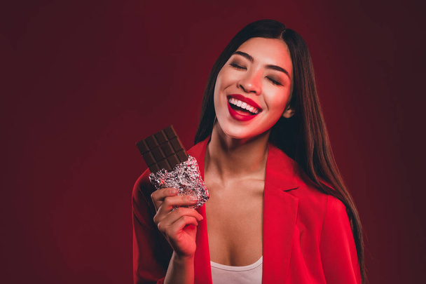Portrait of gorgeous chic trendy cheerful girl eating milk chocolate laughing isolated over bright red light shine color background - Photo, image