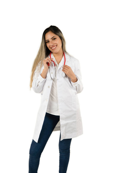 Junge Latina-Ärztin mit breitem Lächeln, die das Stethoskop vor weißem Hintergrund hält. Konzept der professionellen Frau, des Gesundheitspersonals. Amerikanisches Flugzeug, Orientierung im Porträt. - Foto, Bild