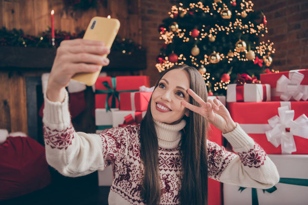 Portrait of attractive cheerful woman making taking slefie showing v-sign festal day time event at decorated loft home indoors - Фото, зображення