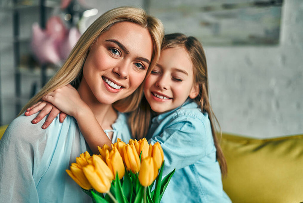 Gelukkige moederdag! Kind dochter feliciteert moeder en geeft haar bloemen tulpen. Mama en meisje glimlachend en knuffelen. Vakantie met het gezin en saamhorigheid. - Foto, afbeelding