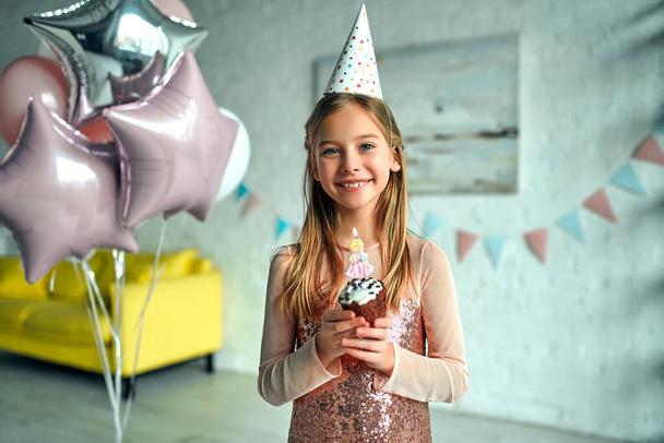 誕生日おめでとう！女の子は誕生日ケーキにろうそくを吹き消す。プリンセスパーティーだ。客室には風船が飾られています。. - 写真・画像