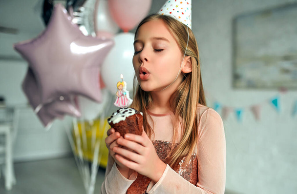 Happy birthday! Girl blowing out candles on birthday cake. Princess party. The room is decorated with balloons. - Foto, Imagem