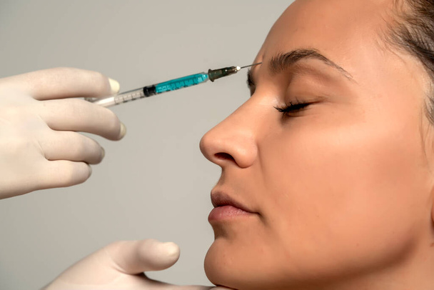 Retrato de uma jovem mulher bonita em um procedimento de injeção de preenchimento facial em fundo cinza - Foto, Imagem