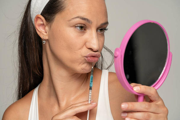 Retrato de una joven mujer hermosa en un procedimiento de autoinyección de relleno de labios sobre fondo blanco - Foto, Imagen