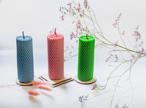 candles made of foundation on the windowsill with dried flowers, three candles of different colors twisted from foundation - Foto, Bild