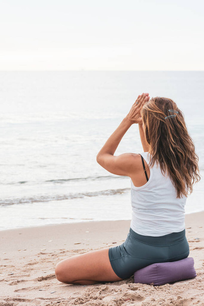 Woman meditating on the beach in anjali mudra, with hands together on forehead, and the sea at background - Foto, imagen
