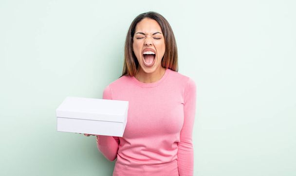 pretty hispanic woman shouting aggressively, looking very angry. white box packaging concept - Zdjęcie, obraz