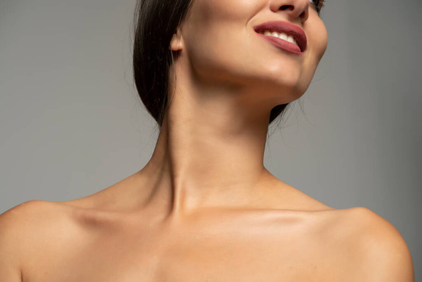 bocca, collo e spalle nude di una donna sorridente su uno sfondo grigio - Foto, immagini