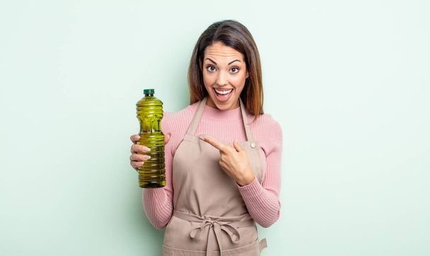 pretty hispanic woman looking excited and surprised pointing to the side. olive oil concept - Photo, image