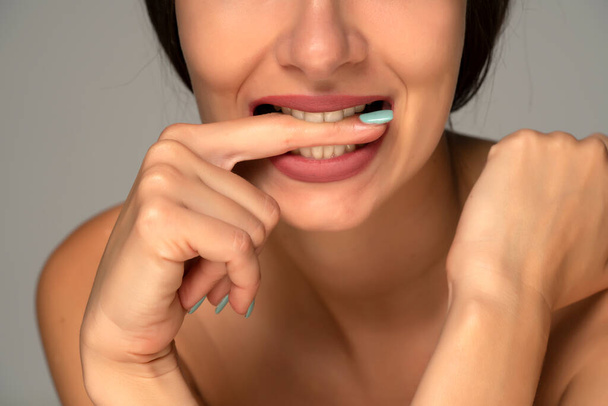 close up retrato de uma jovem mordendo o dedo em um fundo cinza - Foto, Imagem