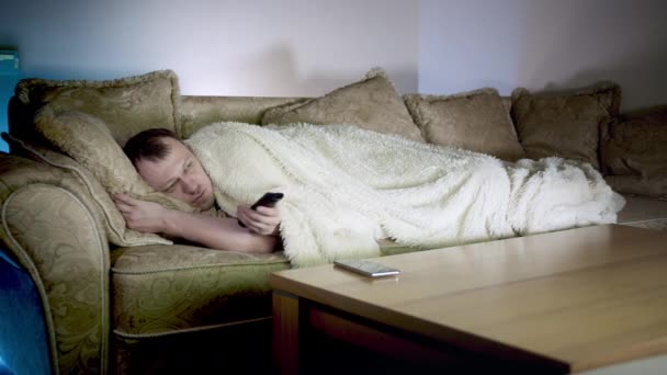 Solitario giovane uomo è sdraiato sul divano a guardare la TV di notte, movimento della fotocamera - Filmati, video