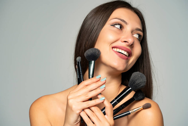 молодая красивая женщина позирует с кистями макияжа на сером фоне - Фото, изображение