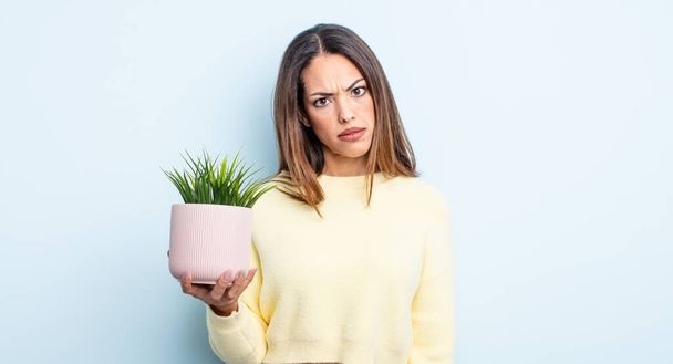 pretty hispanic woman feeling puzzled and confused. houseplant concept - Photo, image