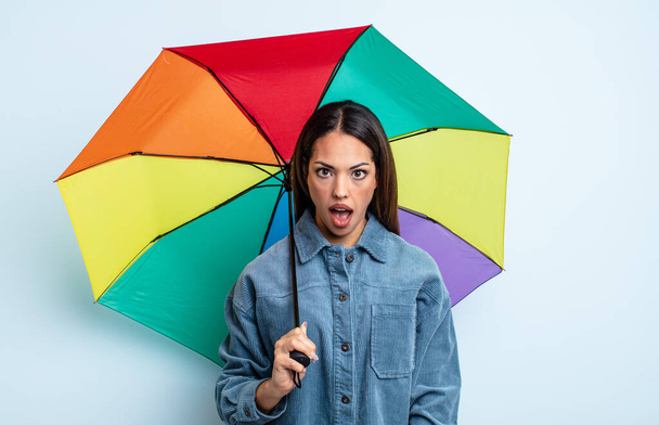pretty hispanic woman looking very shocked or surprised. umbrella concept - Фото, изображение