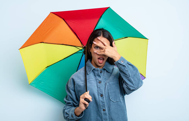 pretty hispanic woman looking shocked, scared or terrified, covering face with hand. umbrella concept - Foto, Imagen