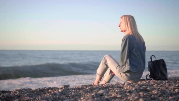 girl is sitting by sea and dreaming. Romantic walk along beautiful shore. - Footage, Video