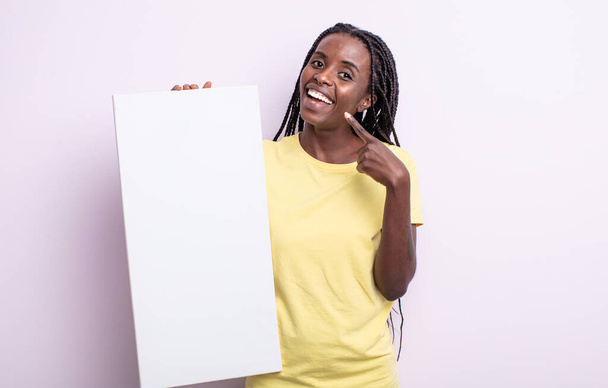 pretty black woman smiling confidently pointing to own broad smile. blank canvas concept - Fotó, kép