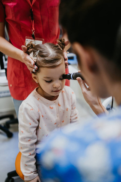 Beautiful and adorable little girl receiving ophthalmology treatment. Doctor ophthalmologist checking her eyesight with modern equipment. - Foto, Imagen