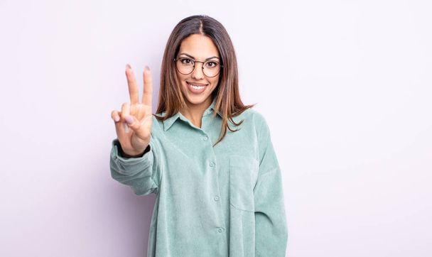 pretty hispanic woman smiling and looking happy, carefree and positive, gesturing victory or peace with one hand - Foto, Imagem