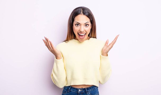 pretty hispanic woman looking happy and excited, shocked with an unexpected surprise with both hands open next to face - Photo, Image