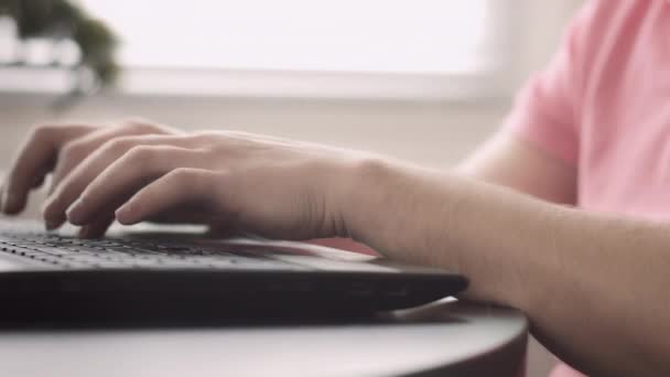 Handen van een man in een roze T-shirt die werkt op een laptop, camera tracking - Video